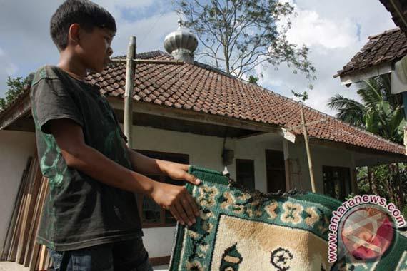 Seorang anak menunjukkan karpet masjid Ahmadiyah yang dibersihkan dan dijemur. (Antara)